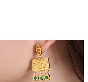 Detail of vintage gold earrings with green gemstones worn on model showing texture