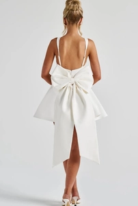 Back view of white spaghetti strap dress featuring a large decorative bow and open back