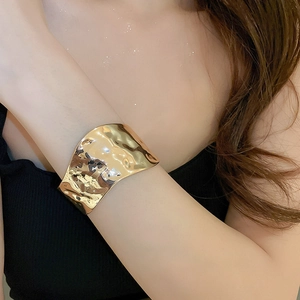 Detailed view of wide gold metal cuff bracelet with unique hammered texture on wrist