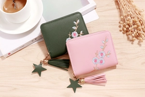 Detailed view of floral embroidery and tassels on PU leather wallets in green and pink