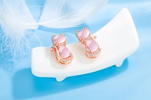 Close-up of pink crystal cat earrings in rose gold finish on a soft blue background