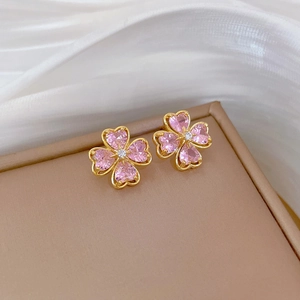 Macro shot of gold four-leaf clover earrings with pink heart stones and a tiny diamond