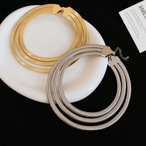 Detail of gold and silver triple-layered flat snake chain necklaces on a ceramic plate