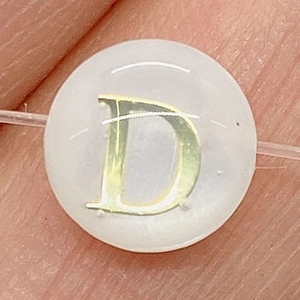 Dettaglio macro di una perla di conchiglia bianca con lettera D dorata per gioielli