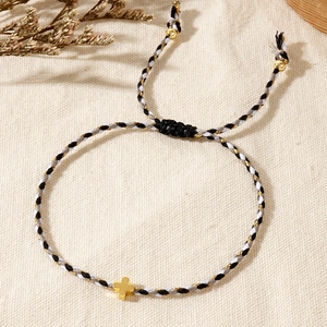 Detail of adjustable braided cord bracelet with a polished gold cross charm on linen fabric