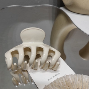 Detail view of cream white hair claw clip with Made in Korea tag on a reflective surface