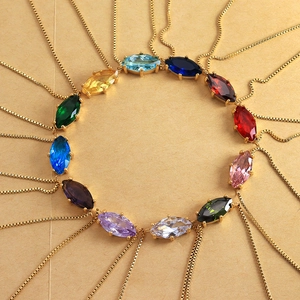 Radial display of colorful marquise gemstone necklaces with golden chains on beige background