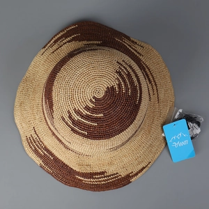 Dettaglio di cappello da sole in rafia bicolore con cordino antivento ed etichetta