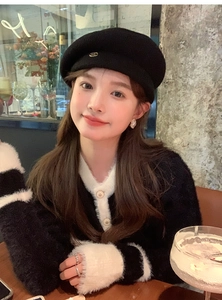 Close-up of black wool beret with metal M letter logo for an elegant autumn look
