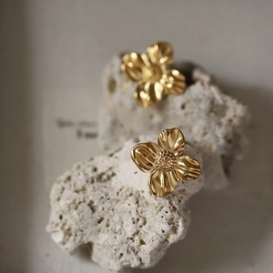 Close-up of golden irregular tropical flower earrings with fine grainy texture on rock