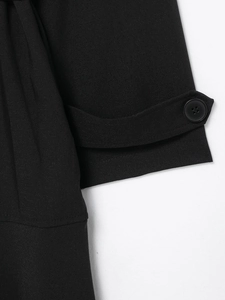 Close-up of black trench dress sleeve detail with classic button and woven fabric texture