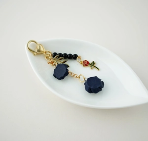 Detail of a golden heart keychain with a red rose and blue flower charms in a white dish