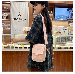 Pink crossbody bag featuring bow embroidery and wide strap shown on a model
