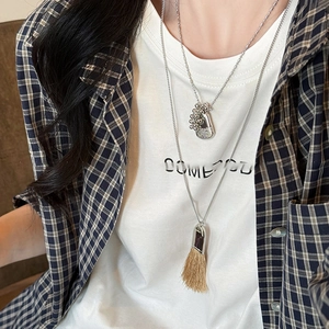 Detail of layered silver necklaces with metallic pendants and khaki tassels on a model