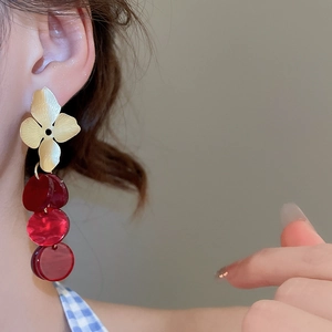 Close-up of matte gold flower earrings with red acrylic discs on a model