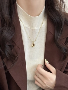 Détail d'un collier vintage doré avec pendentif oeil de tigre sur un pull en maille