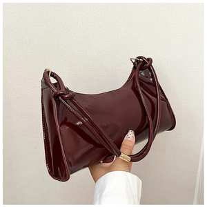 Detail of burgundy patent leather baguette bag with knotted strap and triangular side profile