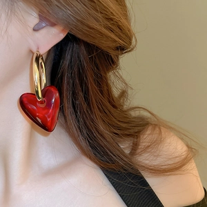 Close-up of a model wearing a gold hoop earring with a red glass heart pendant