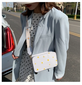 Close-up of white crossbody bag with daisy floral embroidery and decorative strap