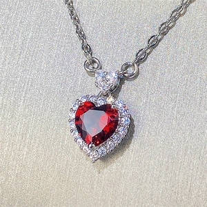 Macro shot of silver heart necklace featuring red gemstone and diamond-set border