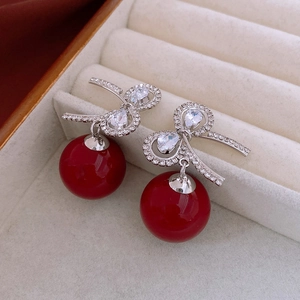 Detailed view of silver bow earrings with red pearls and crystals in a white jewelry box