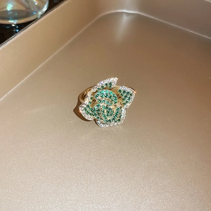 Macro shot of camellia ring with green and clear zircons on a gold tray
