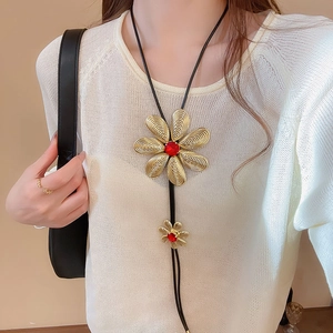 Close-up of golden metal flower pendant with red center gemstone on black rope necklace