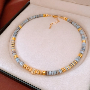 Detail of beaded necklace with gold stripes and grey-blue stone discs in jewelry box