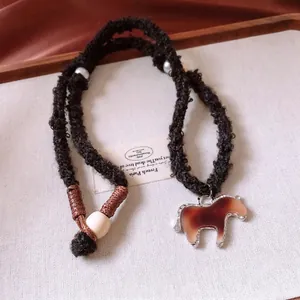 Knitted rope necklace with brown horse pendant and white decorative beads on a beige tray