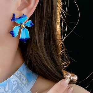 Close-up of blue flower earrings with gold stamens worn by a model in soft lighting