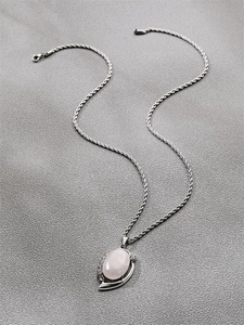 Detail of silver twisted rope chain with an oval pink crystal pendant on grey fabric