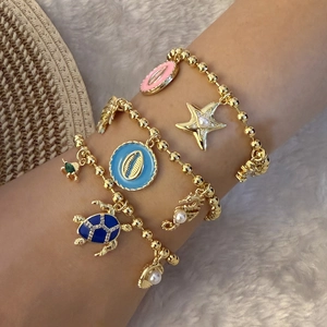 Sommerliche goldene Perlenarmbänder mit blauem Schildkröten- und Seesternanhänger am Handgelenk