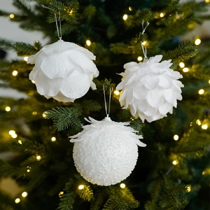 Close-up of white feather-textured Christmas ball ornaments on a warm glowing tree
