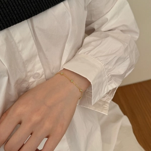 Detail of a gold bracelet with green stones on a model's wrist wearing a white shirt