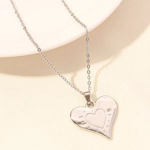 Close-up of heart-shaped silver pendant with minimalist fine chain on white surface