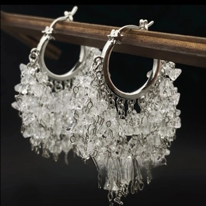 Detailed close-up of silver hoop earrings featuring layered crystal tassels on black background