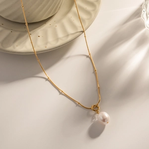 Gold chain necklace featuring natural pearl pendant with delicate metallic beads accent