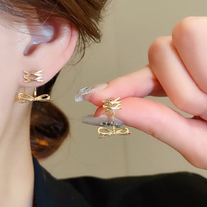 Detailed view of layered gold bow earrings with crystal cross ribbon accents on ear