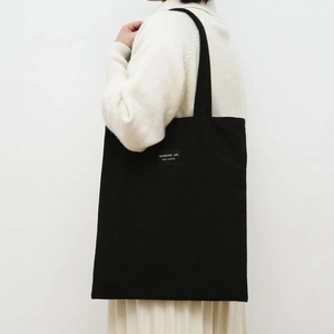 Detail of a black canvas tote bag with a geometric life label and thick shoulder straps