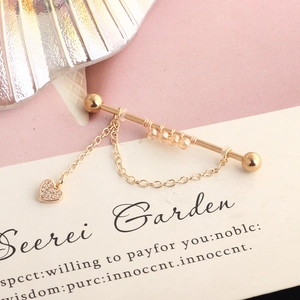 Macro shot of gold industrial barbell earring with crystal heart pendant on pink card