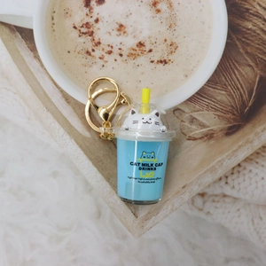 Detail of blue cat milk tea acrylic keychain on wooden tray with white faux fur background