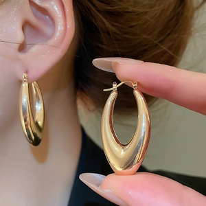 Detailaufnahme goldener U-förmiger Tropfenohrring mit glänzendem Metall-Spiegeleffekt