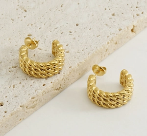 Macro detail of gold-plated twisted rope C-shaped hoop earrings on a stone base