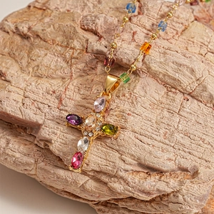 Detailed close-up of a gold cross pendant with colorful rhinestones on a natural rock