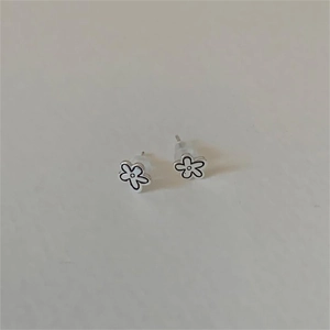 Detail of silver flower stud earrings with black outlines and clear silicone backs