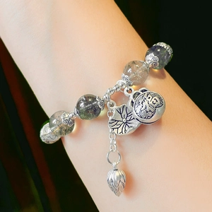 Detailed macro view of the green phantom crystal beads and silver lotus charms on bracelet