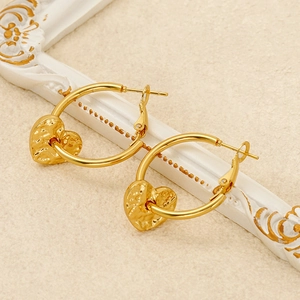 Close-up of golden hammered heart drop earrings on an elegant white relief background