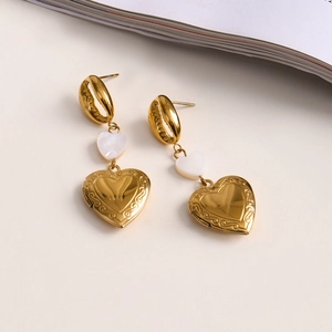 Gold heart drop earrings with white shell inlay and locket pendant on beige table