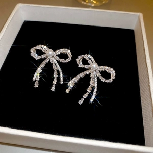 Macro shot of silver bow earrings with sparkling crystals and pearl drops on black velvet