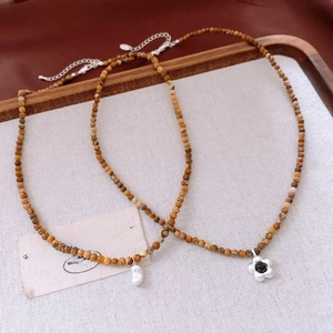 Détail de colliers perlés avec perles baroques et breloques de fleurs sur fond lin
